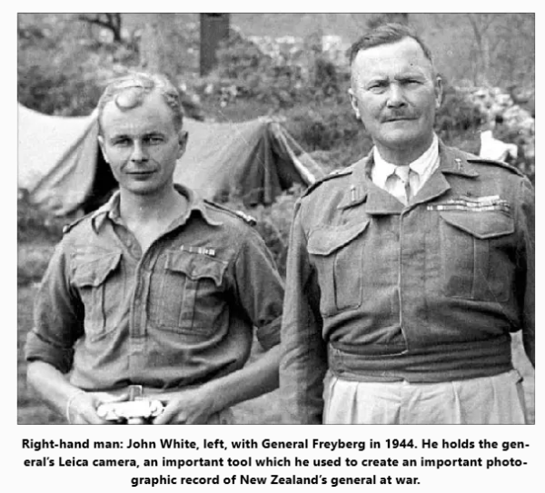 A black and white photograph showing two men facing the camera. They are in army uniform and John White, on the left, is holding a camera.